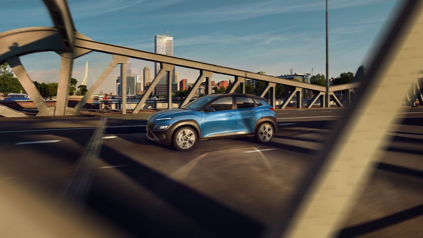 Nový Hyundai KONA ze strany v barvě Surfy Blue, přejíždějící most.