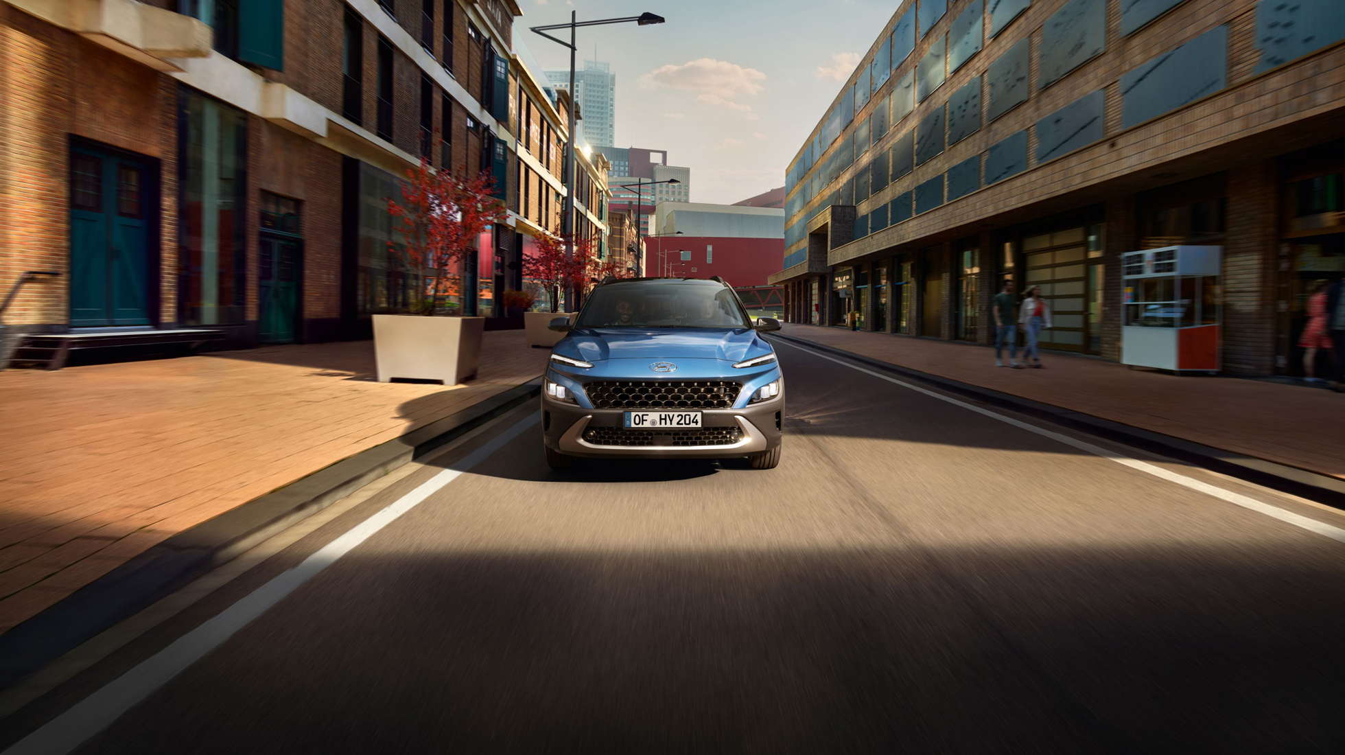 Pohled zepředu na nový Hyundai Kona Hybrid v modrém odstínu Surfy Blue, jedoucí ve slunečním světle.
